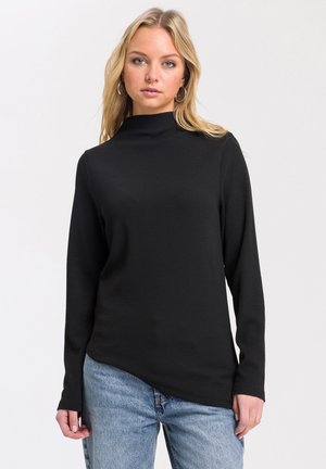 Czarny top z long-sleeve, z wysokim kołnierzem, prążkowaną teksturą i lekko asymetrycznym dołem, w zestawieniu z jasnoniebieskimi dżinsami.