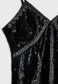 Schwarzes Samtkleid mit einer strukturierten Oberfläche, verziert mit Perlenakzenten entlang des Halsausschnitts und verstreuten Pailletten für Detail. Träger im Spaghettistil.