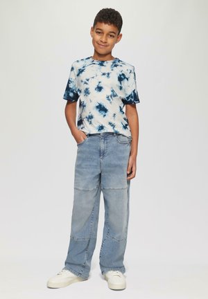 Tie-dye t-shirt met korte mouwen in wit en marineblauw, gecombineerd met lichtblauwe wijde jeans met patchwork naden, en witte sneakers.