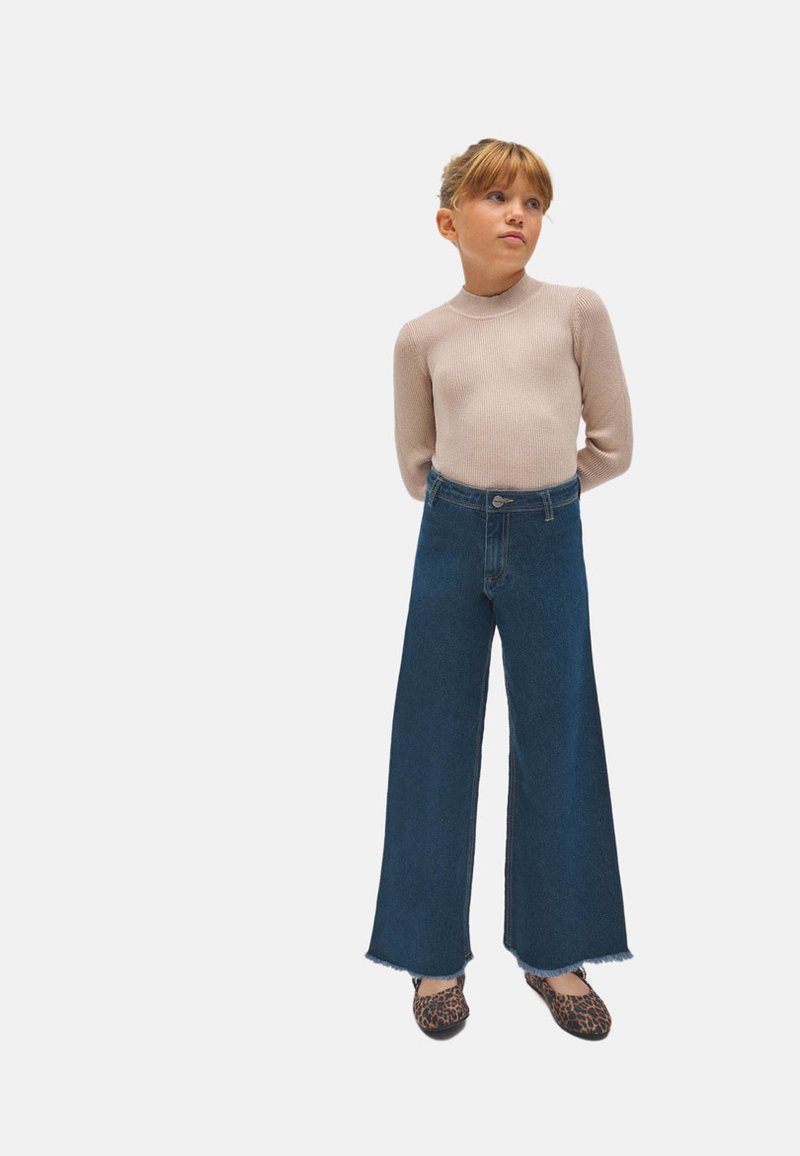 Top de manga larga acanalada en beige claro, vaqueros de tiro alto y pierna ancha en denim oscuro con dobladillo sin terminar, y zapatos planos con estampado de animal.