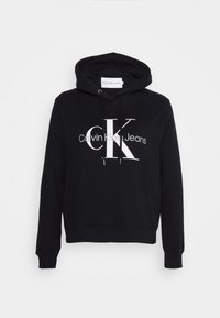 Juodas džemperis su kengūros kišene, su raišteliu ant gyvatuko ir ryškiu baltu "CK" logotipu su tekstu "Calvin Klein Jeans" po juo. Minkšta medžiaga.