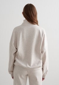 Sudadera beige claro con cuello alto y puños acanalados. Corte suelto, textura suave, combinada con pantalones a juego.