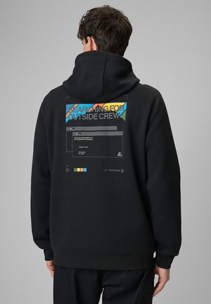 Mężczyzna w czarnej bluzie z kapturem z kolorowym napisem "SEARCHING FOR OUTSIDE CREW" i graficznym wzorem okien na plecach, zwrócony tyłem.