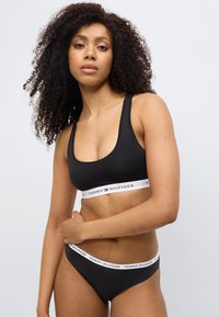 Μαύρο βαμβακερό σουτιέν bralette και ταιριαστό σλιπ με λευκή λωρίδα λογότυπου. Το σχέδιο διαθέτει λαιμόκοψη scoop και χαμηλή μέση.