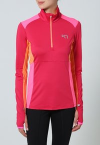 Długi rękaw sportowa koszulka z półzamkiem, głównie różowa z pomarańczowymi i jaśniejszymi różowymi akcentami, wykonana z gładkiego, rozciągliwego materiału.