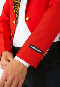 Czerwony żakiet z złotymi guzikami, z czarną i złotą wzorzystą podszewką. Czarny metka "SUITMEISTER" na mankiecie z białą koszulą pod spodem.