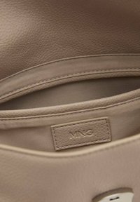 Beige leren handtas interieur met gestructureerd oppervlak, gestikte details en een merklabel. Glad voering en een discreet vak.