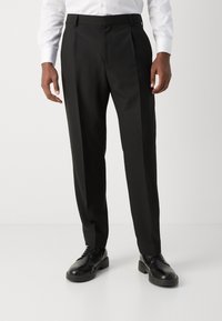 Schwarze maßgeschneiderte Hosen mit geradem Schnitt, ausgestattet mit Vorderfalten, einer glatten Textur und seitlichen Taschen, kombiniert mit schwarzen eleganten Schuhen.