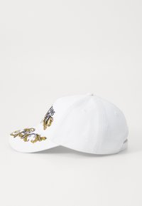 Cappellino da baseball bianco con motivi floreali ricamati in oro e nero sulla visiera e sulla parte anteriore. Presenta una forma strutturata e una chiusura regolabile.