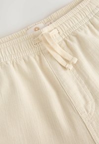 Shorts élastiques beige clair à taille élastique avec cordon de serrage, dotés d'un tissu texturé subtil et d'une poche avant unique.