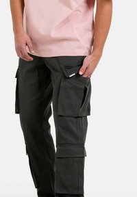Zwarte cargobroek van stof met meerdere zijzakken, gestikte details en een losse pasvorm, gecombineerd met een lichtroze t-shirt.