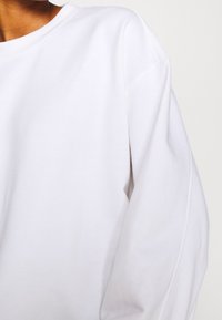 Witte sweatshirt met een ronde hals, verlaagde schouders en een zachte stof met een gladde textuur. Zichtbare stikseldetails op de mouwen.