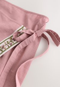 Delantal de lino rosa atado con un lazo, con una franja blanca con bordado floral verde y rosa a lo largo del borde.