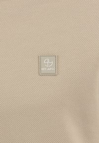 Textil beige con una textura acanalada que presenta una etiqueta rectangular gris con el texto "KEY LARGO" en blanco, posicionada en el centro.