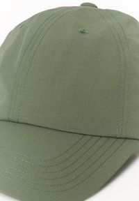 Casquette verte en tissu texturé avec des coutures visibles et une visière légèrement courbée. Elle comporte six œillets de ventilation et une couronne arrondie.