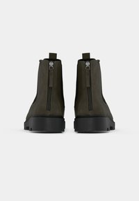 Olivenfarbene Stiefeletten mit glatter Textur, ausgestattet mit zwei seitlichen Reißverschlüssen und einer schwarzen Gummisohle für besseren Halt.