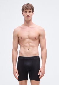 Čierne boxerky s hladkou textúrou, vybavené širokým elastickým pásom. Strih je priliehavý, zdôrazňujúci moderný dizajn a jednoduchý štýl.