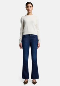 Maglione bianco a maglia, jeans svasati blu scuro e scarpe marroni con motivo. L'outfit presenta un design semplice e una vestibilità classica.