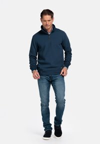 Donker marineblauwe quarter-zip pullover met een gestructureerd oppervlak, gecombineerd met lichtblauwe denim jeans en zwarte casual schoenen.