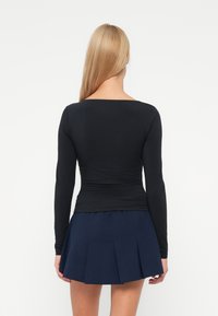 Top negru cu mânecă lungă, cu decolteu rotund și textură strânsă la talie, asortat cu o fustă mini plisată de culoare bleu închis.