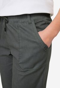 Szare legginsy z elastycznym paskiem w talii i sznurkiem do regulacji. Posiadają boczne kieszenie, teksturowany materiał oraz charakterystyczną metkę marki na kieszeni.