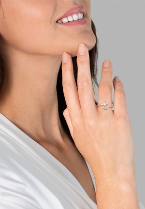 Silberner Ring mit floralem Design und strukturiertem Band, getragen an einer Hand mit neutralem Nagellack vor einem hellen Hintergrund.