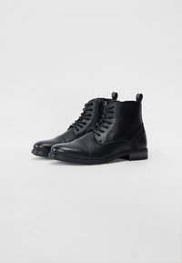 Stivaletti in pelle nera con punta tonda, chiusura con lacci frontale, zip laterale, tacco basso e linguetta sul retro.