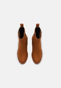 Stivali ankle in suede marrone con una texture liscia, cerniera laterale e linguette per il tiraggio, caratterizzati da una punta arrotondata e una sottile suola in gomma.