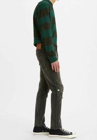 Camisa de manga larga a rayas verdes y negras, combinada con jeans oscuros desgastados de color gris y zapatillas altas negras con suelas blancas.