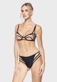 Zwart lingerie set met transparante panelen, ingewikkeld strapdesign en uitsparingen op de bikini-bodem, wat een moderne en gedurfde uitstraling biedt.