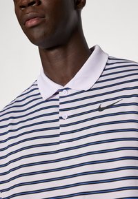 Striped polo shirt in purple, white, and blue. Features a black Nike logo, two buttons at the collar, and a textured fabric.