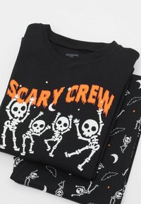 Schwarzes T-Shirt mit kurzen Ärmeln, versehen mit weißen Skelettgrafiken und dem Text "SCARY CREW" in fett orange. Hergestellt aus weichem Baumwollmaterial, lässiges Design.