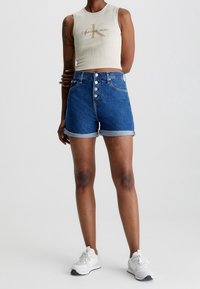 Shorts in denim blu scuro con orli arrotolati, chiusura frontale a cinque bottoni e cuciture a contrasto. Abbinati a un top leggero e aderente senza maniche.