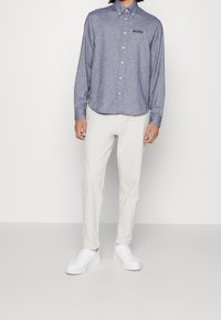 Světle modrá košile na knoflíky s límečkem, zdobená vyšitým logem "BOSS". Barevně doplněna krémovými kalhotami a bílými teniskami.