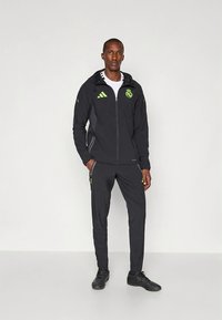 Black athletic tracksuit with green accents, featuring a zip-up jacket and matching pants. Made of lightweight material, includes Adidas branding.