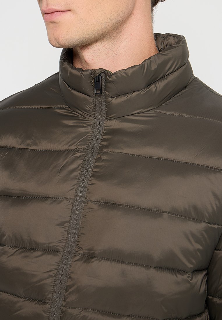 Chaquetón de color verde oliva oscuro y puffy, hecho de un material ligero y brillante, con costuras horizontales, cuello alto con cremallera y sin hardware visible.