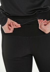 Leggings de sport noirs avec une taille haute et une poche zippée dissimulée. Tissu lisse et extensible ; coutures plates garantissant un confort optimal.