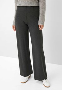Hochtaillierte, weit geschnittene Hose aus dunkelgrauem Stoff. Mit Fronttaschen und einer glatten Textur. Kombiniert mit weißen Schuhen.