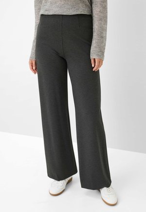 Hoge taille, wijde pijpen broek van donkergrijze stof. Bevat voorzakken en heeft een gladde textuur. Gepaard met witte schoenen.