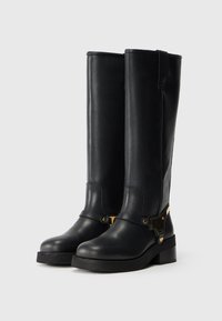 Cizme negre înalte, din piele netedă, cu un accent de cataramă aurie și o talpă din cauciuc chunky. Designul este simplu și elegant.
