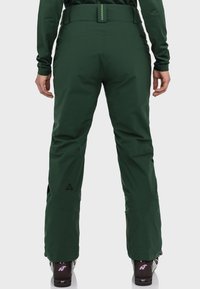 Grüne Skihosen mit glatter Textur, hohem Bund, dezentem Branding und schmal zulaufendem Schnitt. Verstärkte Öffnungen an den Knöcheln.
