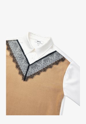 Pull beige avec bordure en dentelle noire et col blanc. La dentelle présente un motif floral. Étiquette visible au niveau du col avec le nom de la marque.