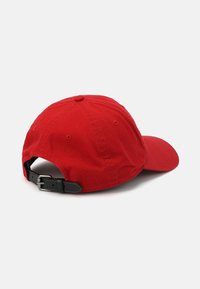 Casquette de baseball en coton rouge avec un bord incurvé, une sangle noire réglable à boucle et des détails de couture visibles sur le couronnement et le bord.