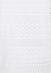 Vit spetstyg med intrikata mönster som innehåller cirklar, diamanter och geometriska designer, som visar en genomskinlig textur genom hela tyget.