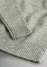 Vaaleanharmaa neulepusero, jossa on pehmeä pinta, joustavat hihansuut ja helma, sekä hienovarainen kirjava kuvio, joka tuo lisävisuaalista kiinnostavuutta.