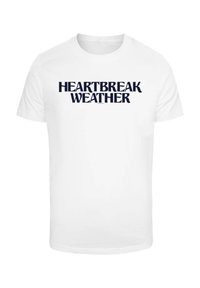Hvit bomull T-skjorte med kraftig marineblå tekst som står "HEARTBREAK WEATHER." Klassisk t-skjorte med rund hals og korte ermer.