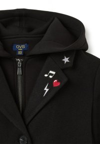 Zwarte rits hoodie met een capuchon, voorzien van een geborduurde zilveren ster, muzikale noot, rode hart en bliksemschicht op de kraag.