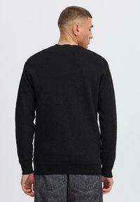 Black knitted sweater with long sleeves, crew neckline, and ribbed cuffs. No visible patterns or hardware. Simple, solid design.