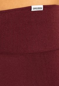 Bordowe legginsy z prążkowanym pasem w talii, z białą metką oznaczoną "SMILODOX" na górze, wykonane z miękkiego, elastycznego materiału.