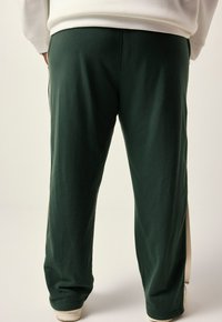 Dark green, loose-fitting sweatpants made of soft fabric, featuring a side stripe detail and elasticated cuffs.